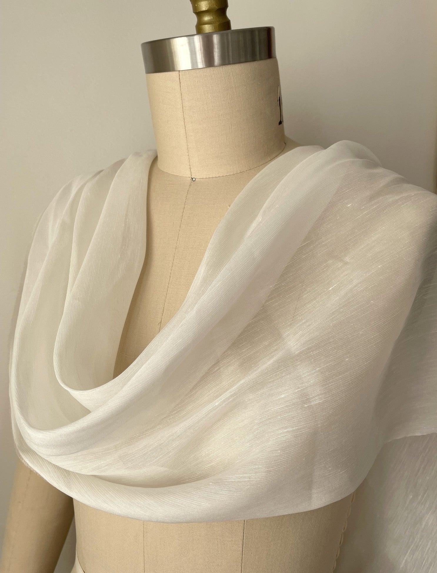 A lightweight, semi-sheer undyed white silk linen fabric draped over a beige fabric dress form mannequin.