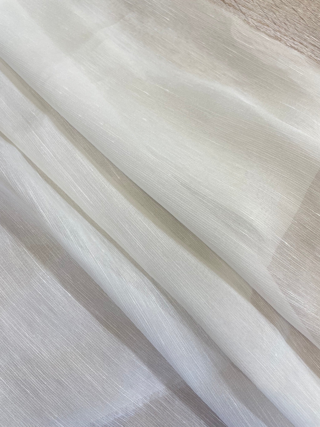A close-up of folded undyed white sheer silk linen fabric with a subtle shimmer, showing its texture and semi-transparency.