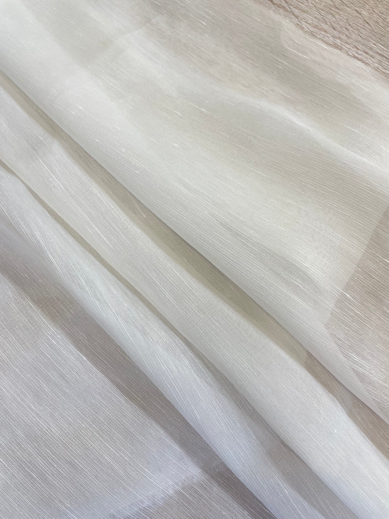 A close-up of folded undyed white sheer silk linen fabric with a subtle shimmer, showing its texture and semi-transparency.