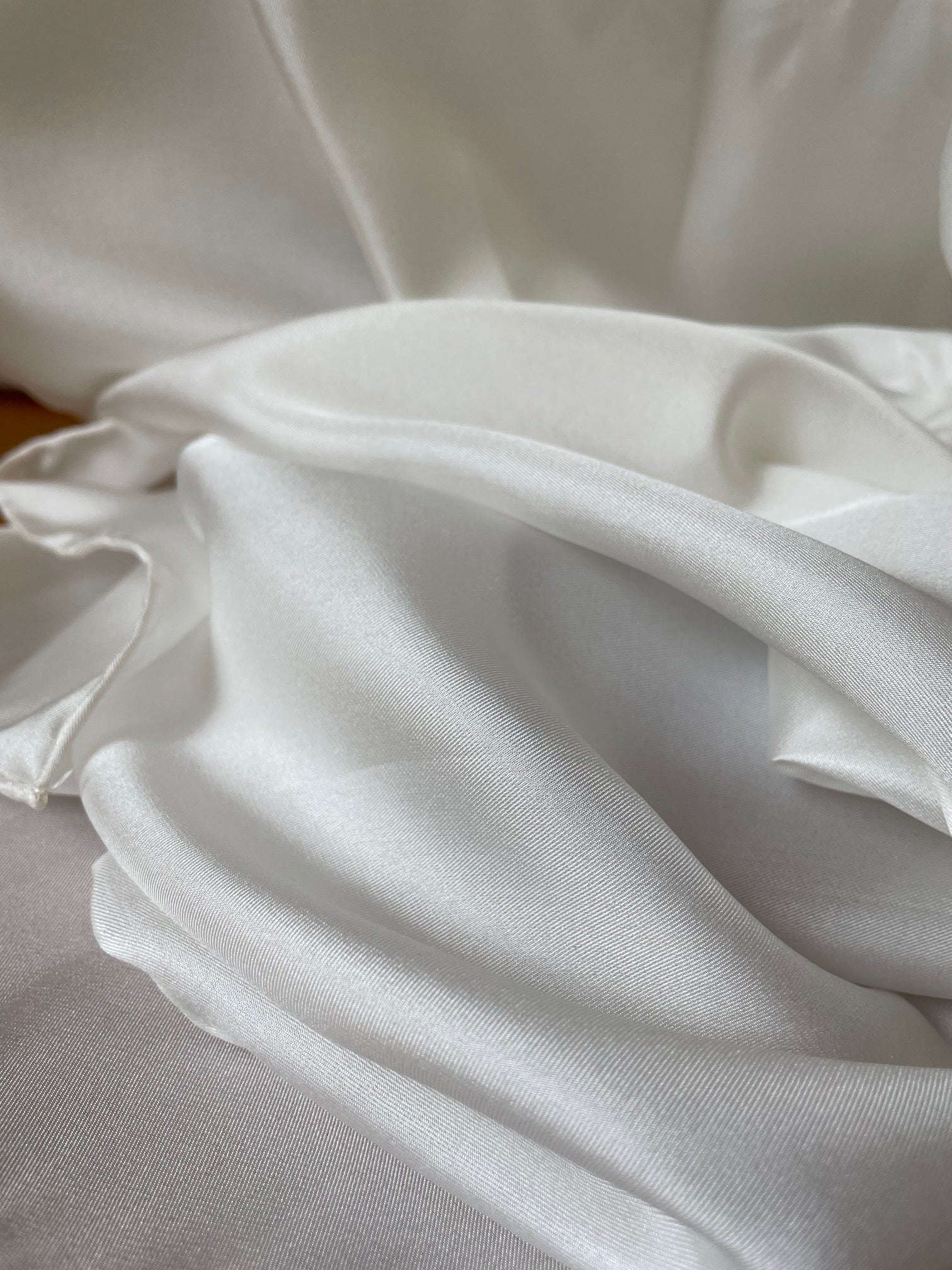 Close-up of undyed white silk twill scarf with folds on a neutral background