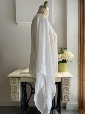 Mannequin draped in undyed silk chiffon top near a sewing machine table with a vase of flowers in the background.