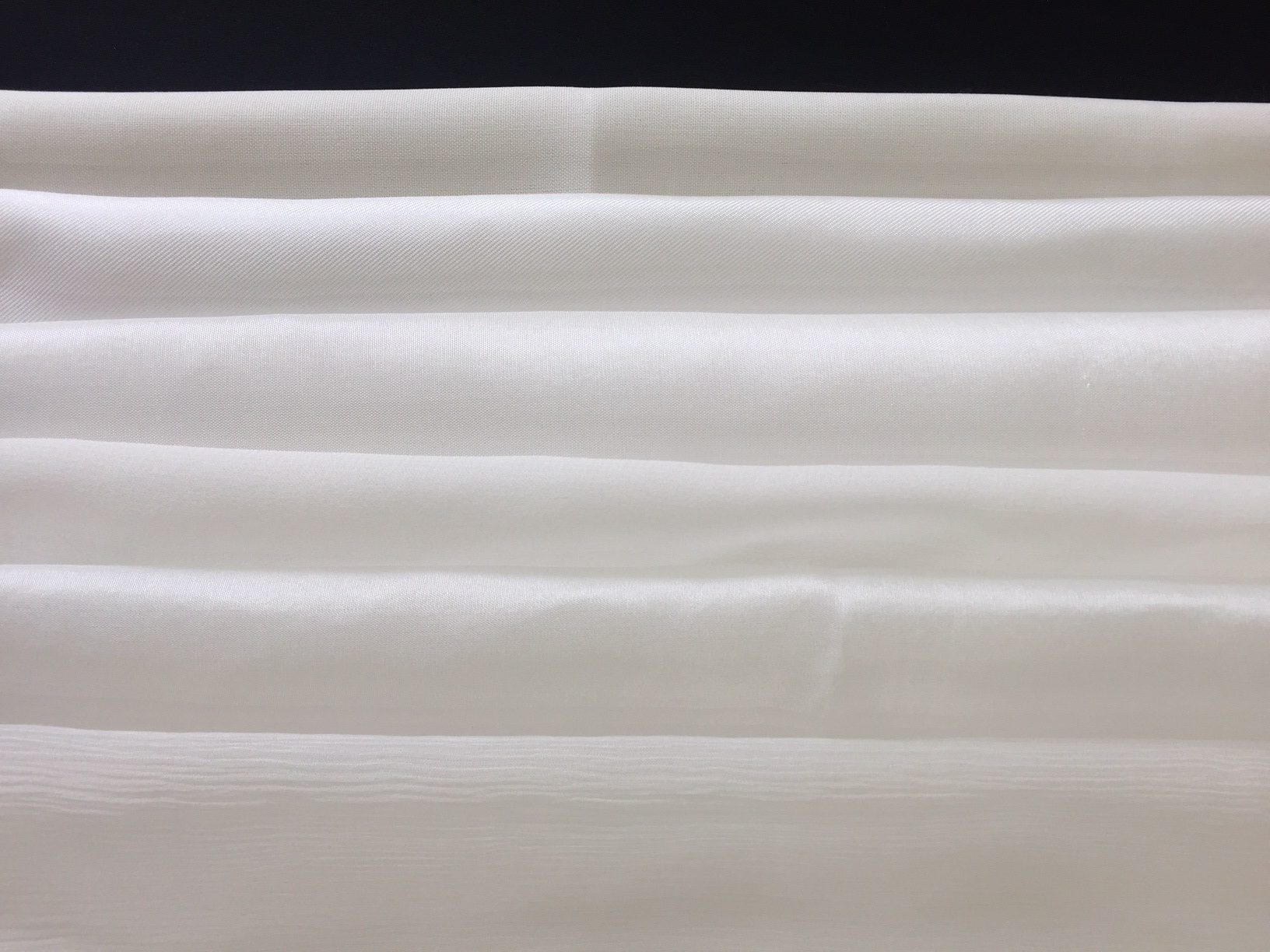 Close-up of undyed white fabric with folds on a black background