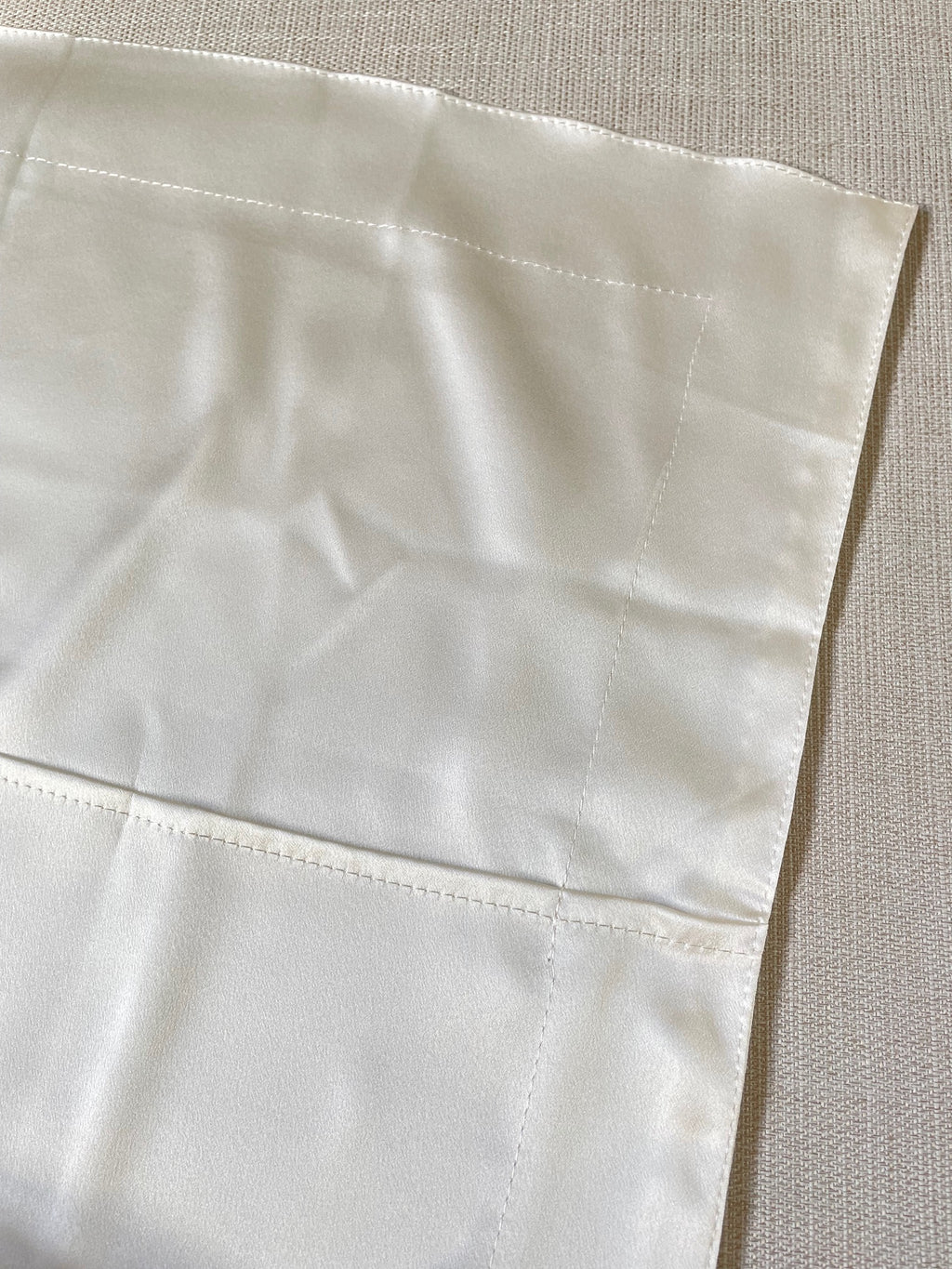 Close-up of a undyed silk satin pillowcase closure with a textured pattern on a neutral background