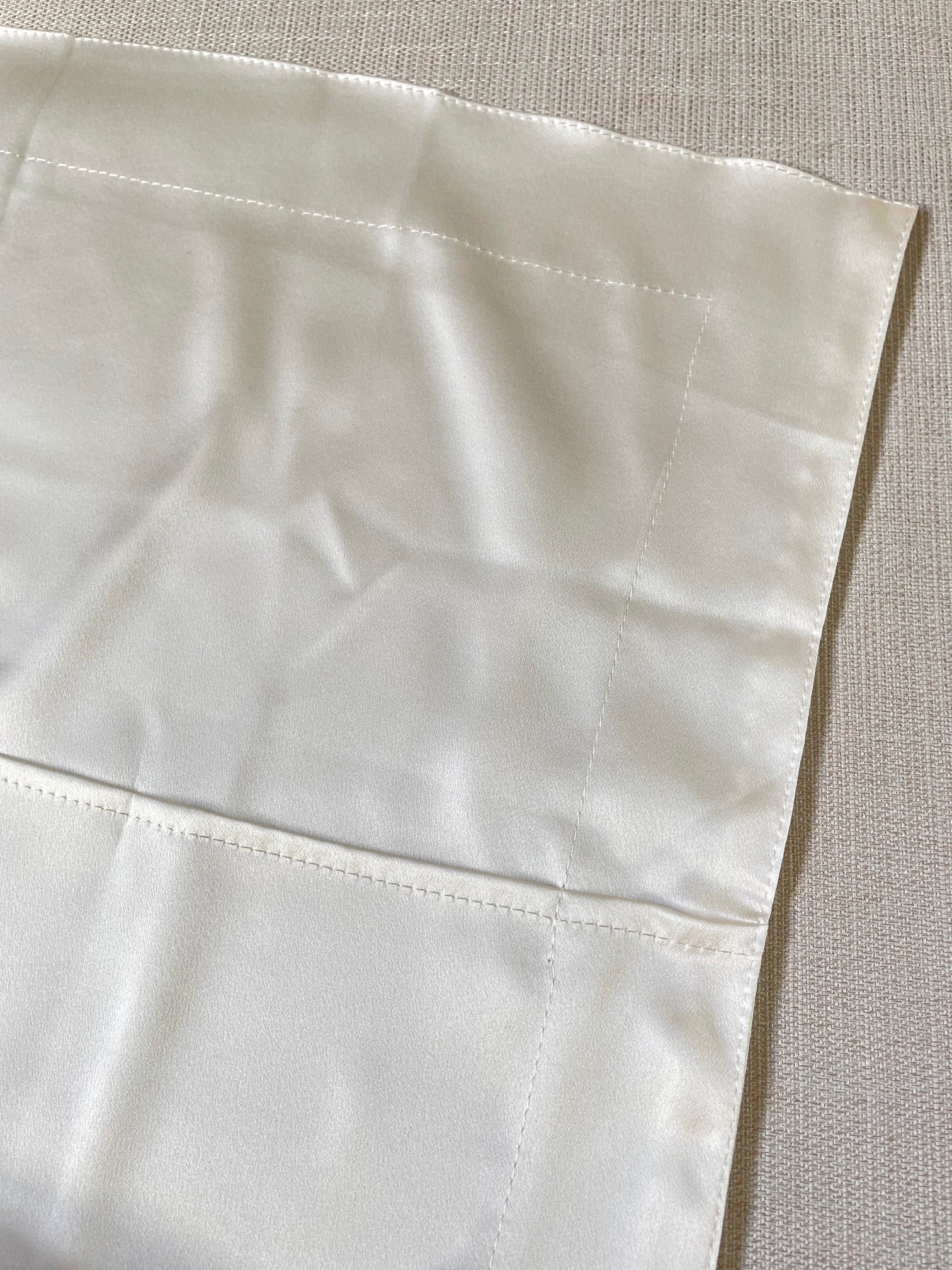 Close-up of a undyed silk satin pillowcase closure with a textured pattern on a neutral background
