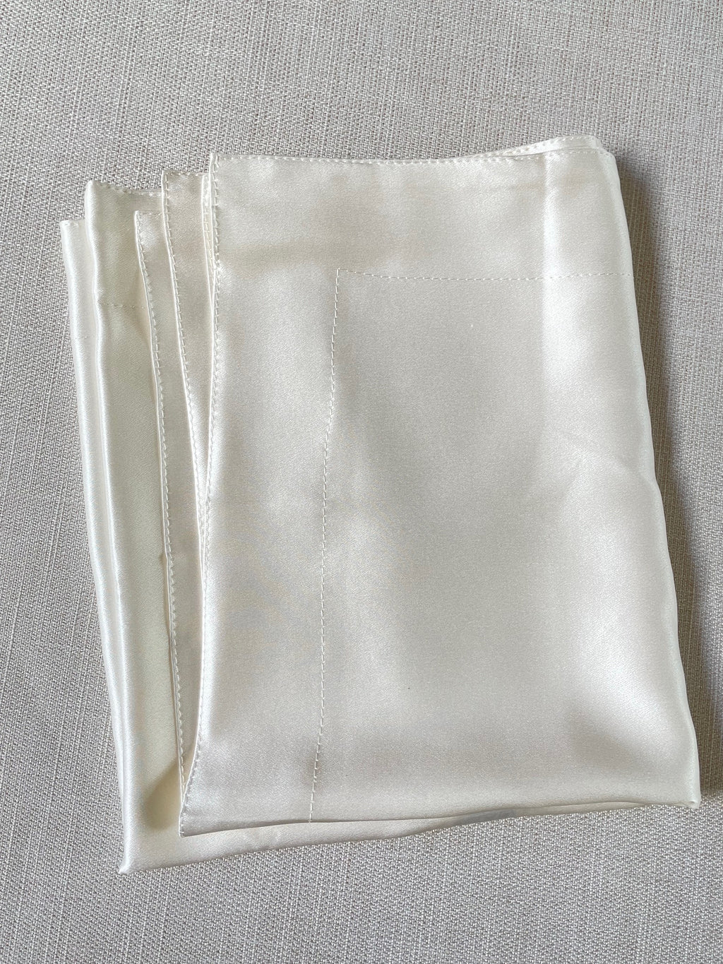 Undyed silk satin pillowcase folded on a gray surface