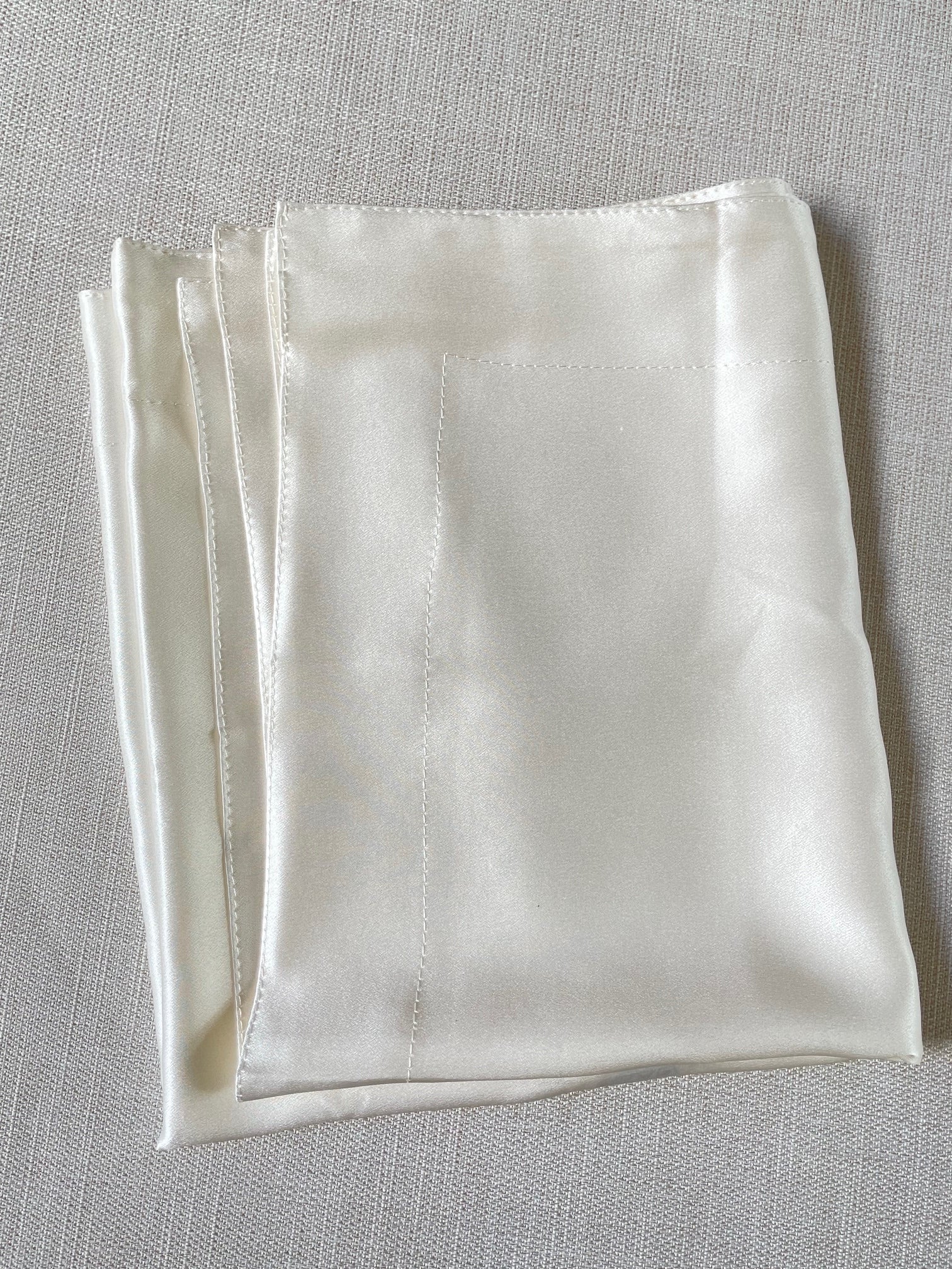 Undyed silk satin pillowcase folded on a gray surface