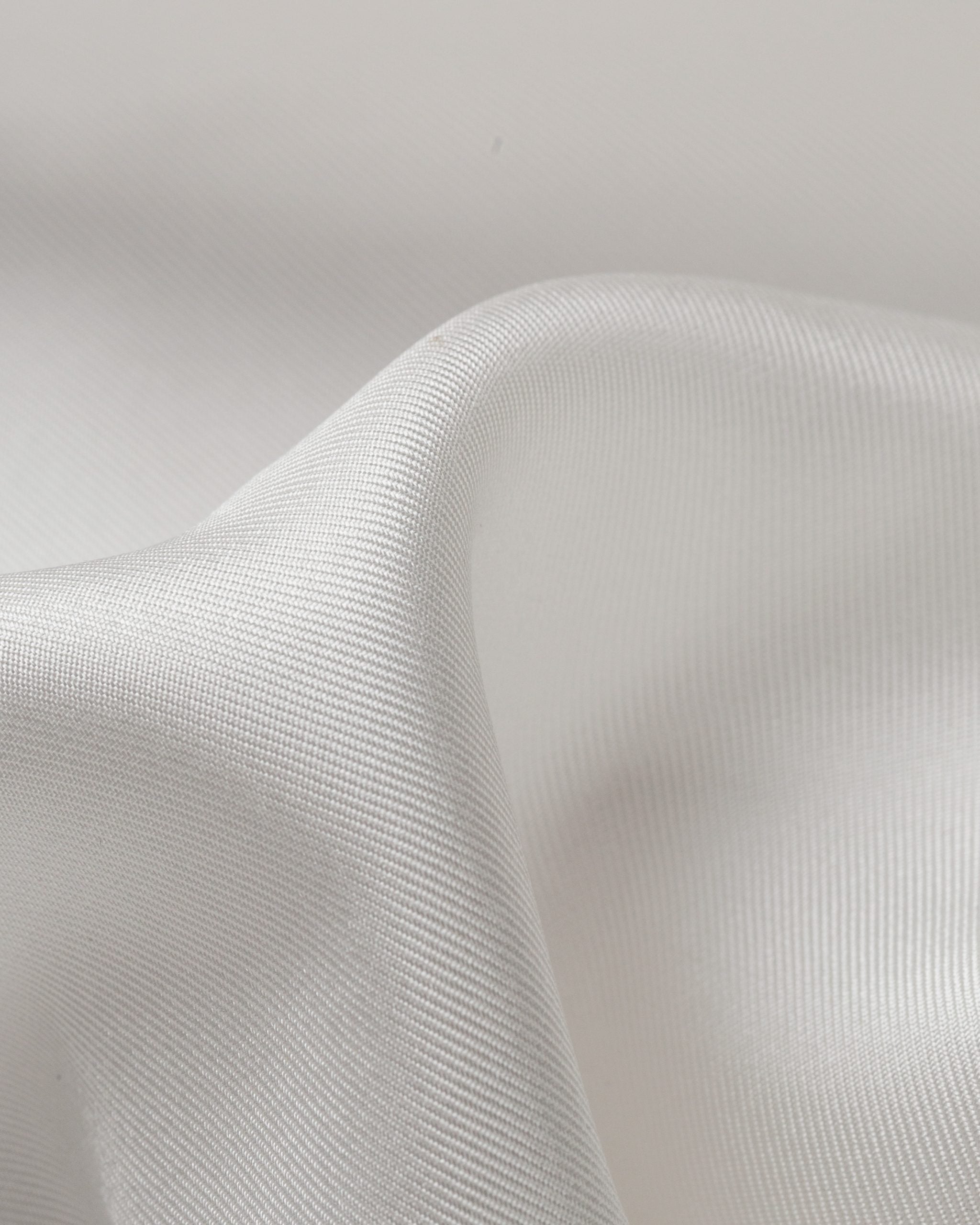 Close-up of undyed silk twill white fabric with a subtle texture on a light gray background