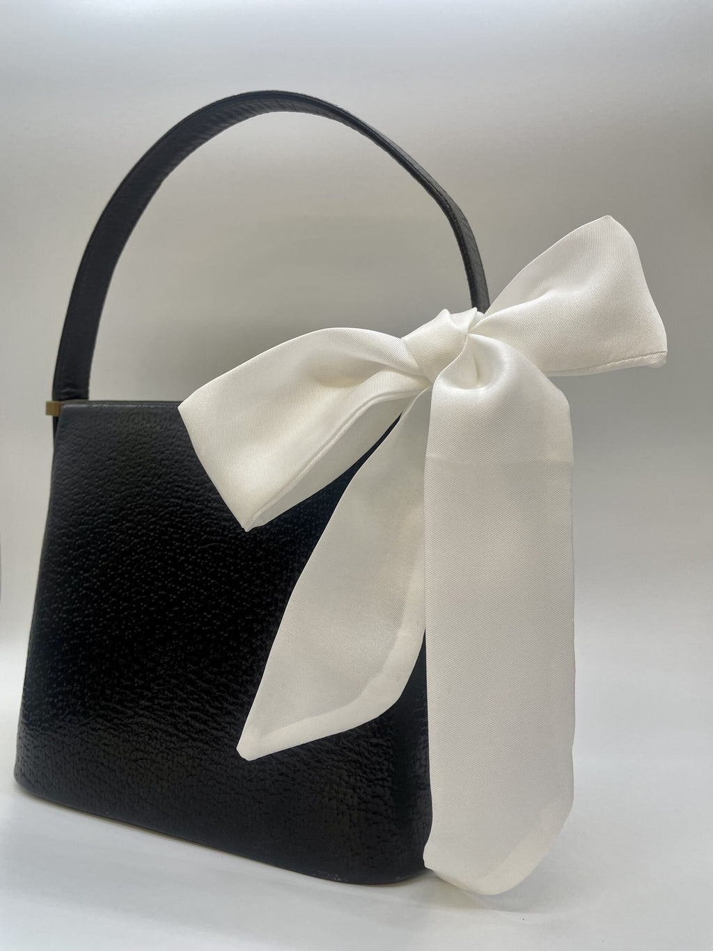 Black handbag with a large white bow on a light gray background