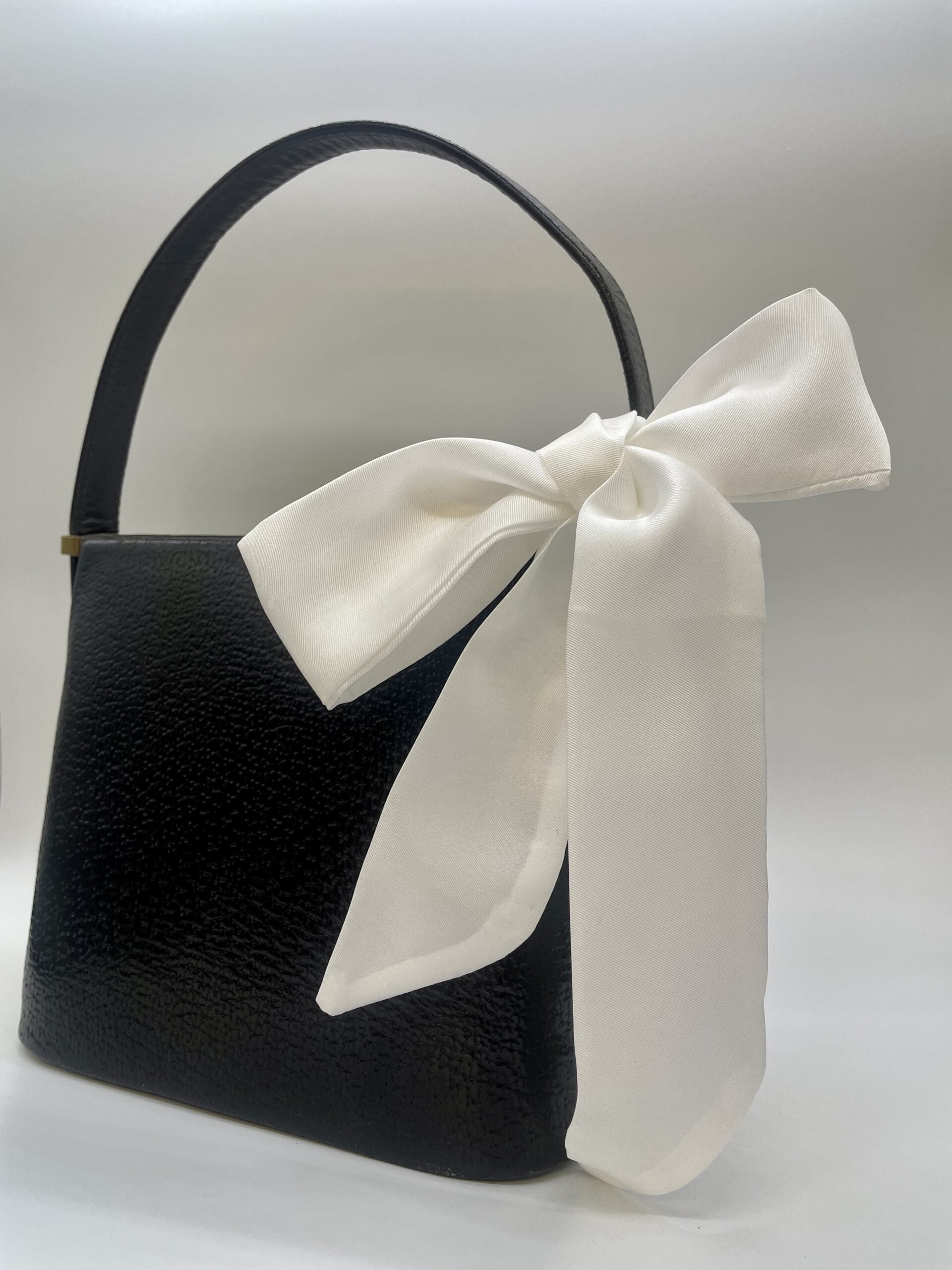 Black handbag with a large white bow on a light gray background