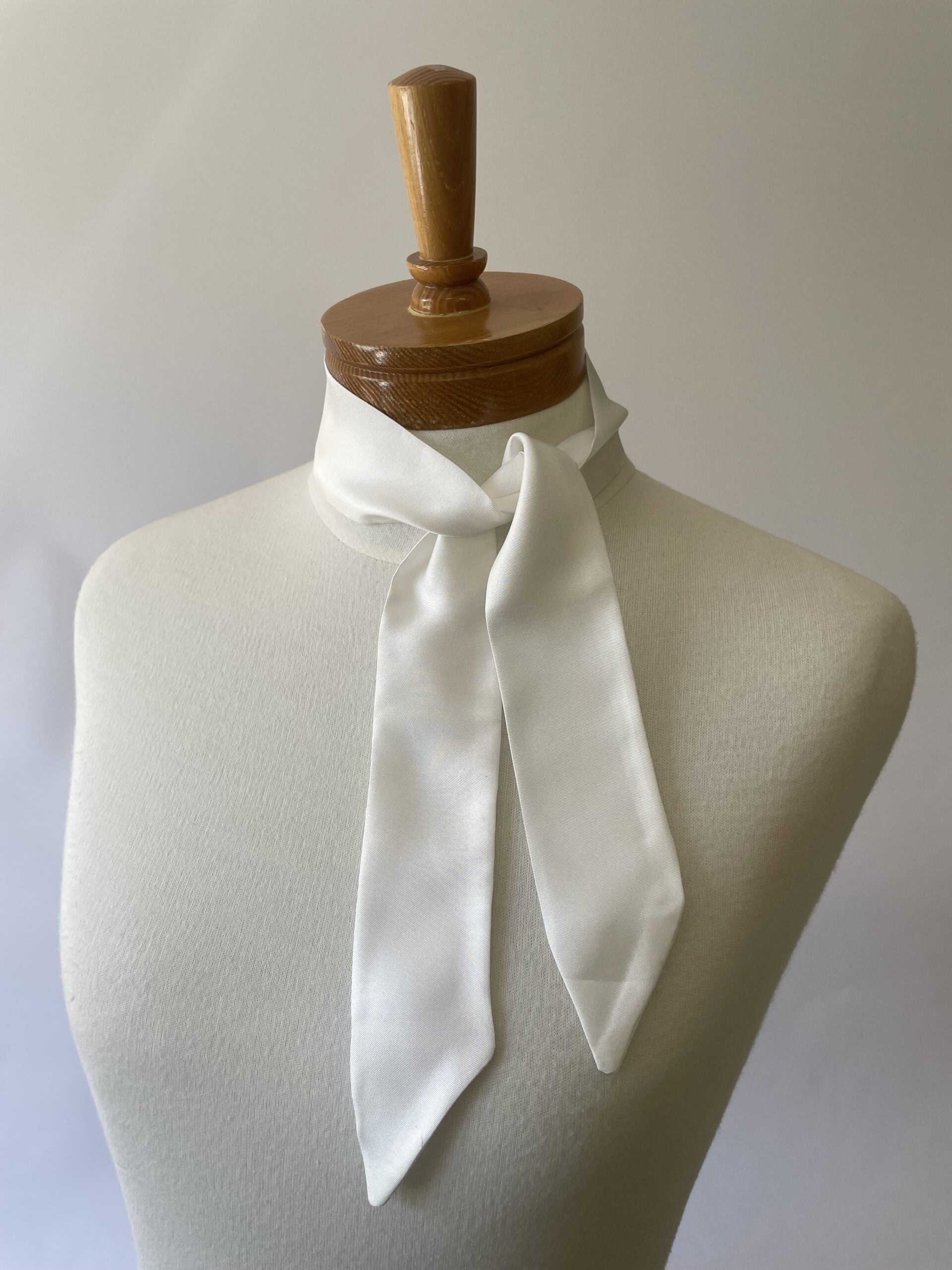 Undyed silk twill twilly scarf draped over a mannequin bust with a wooden headrest against a plain background