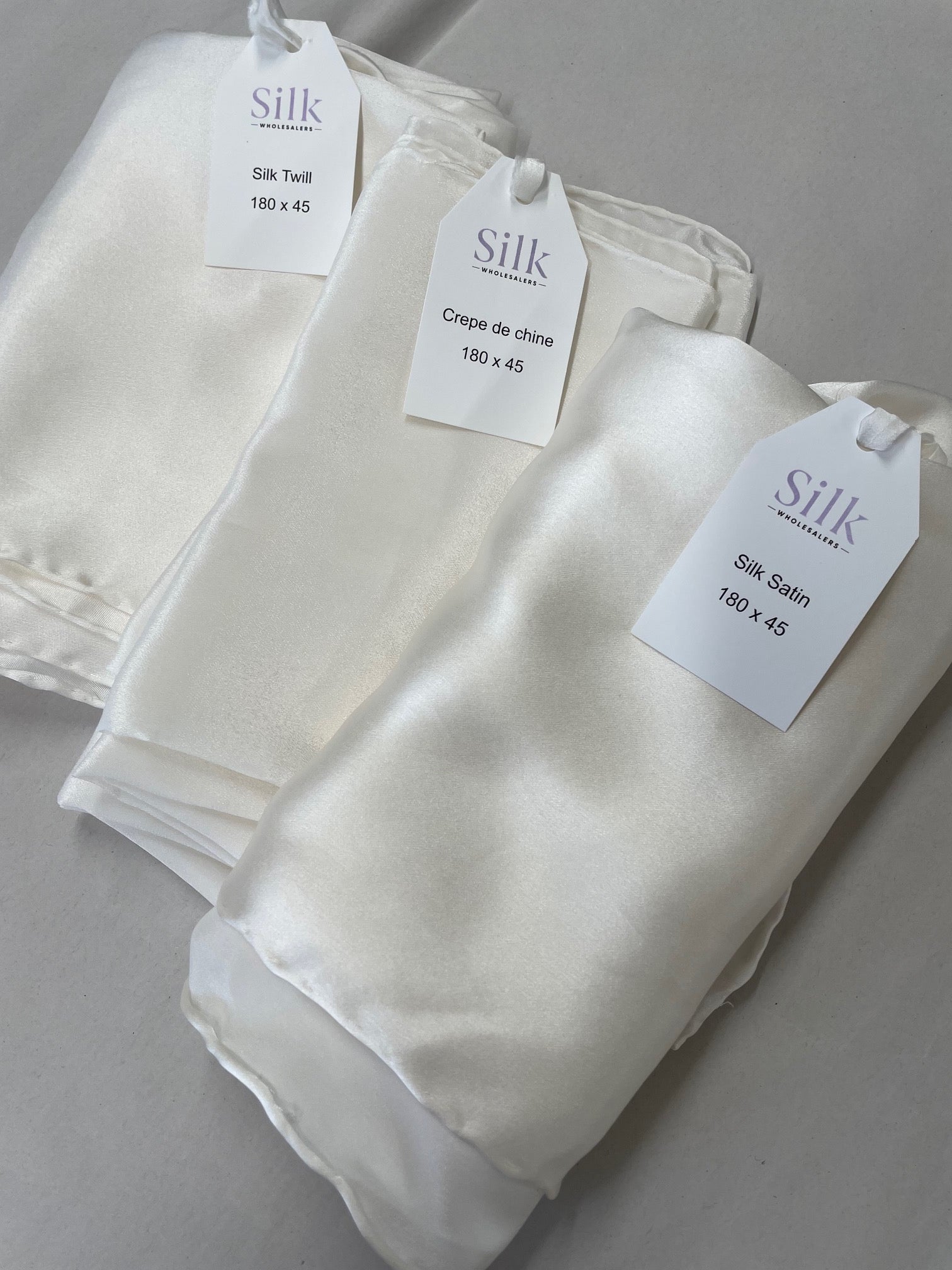 Folded Undyed silk scarves with tags on a gray background