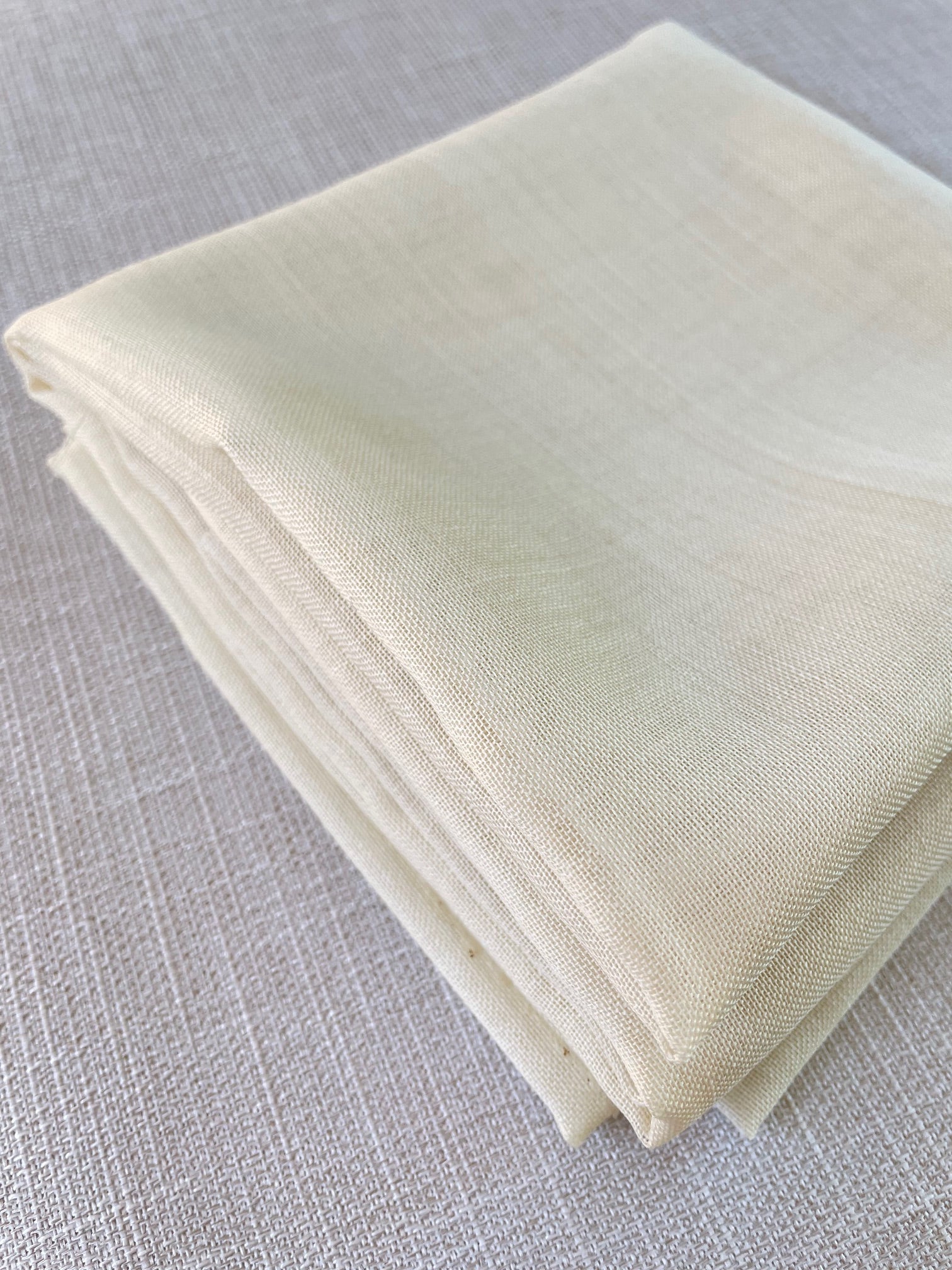 Folded undyed wool gauze fabric on a textured gray surface