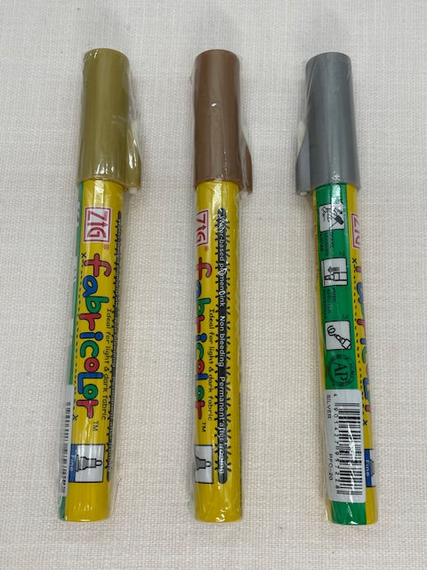 Three Zig fabric color markers on a textured white background