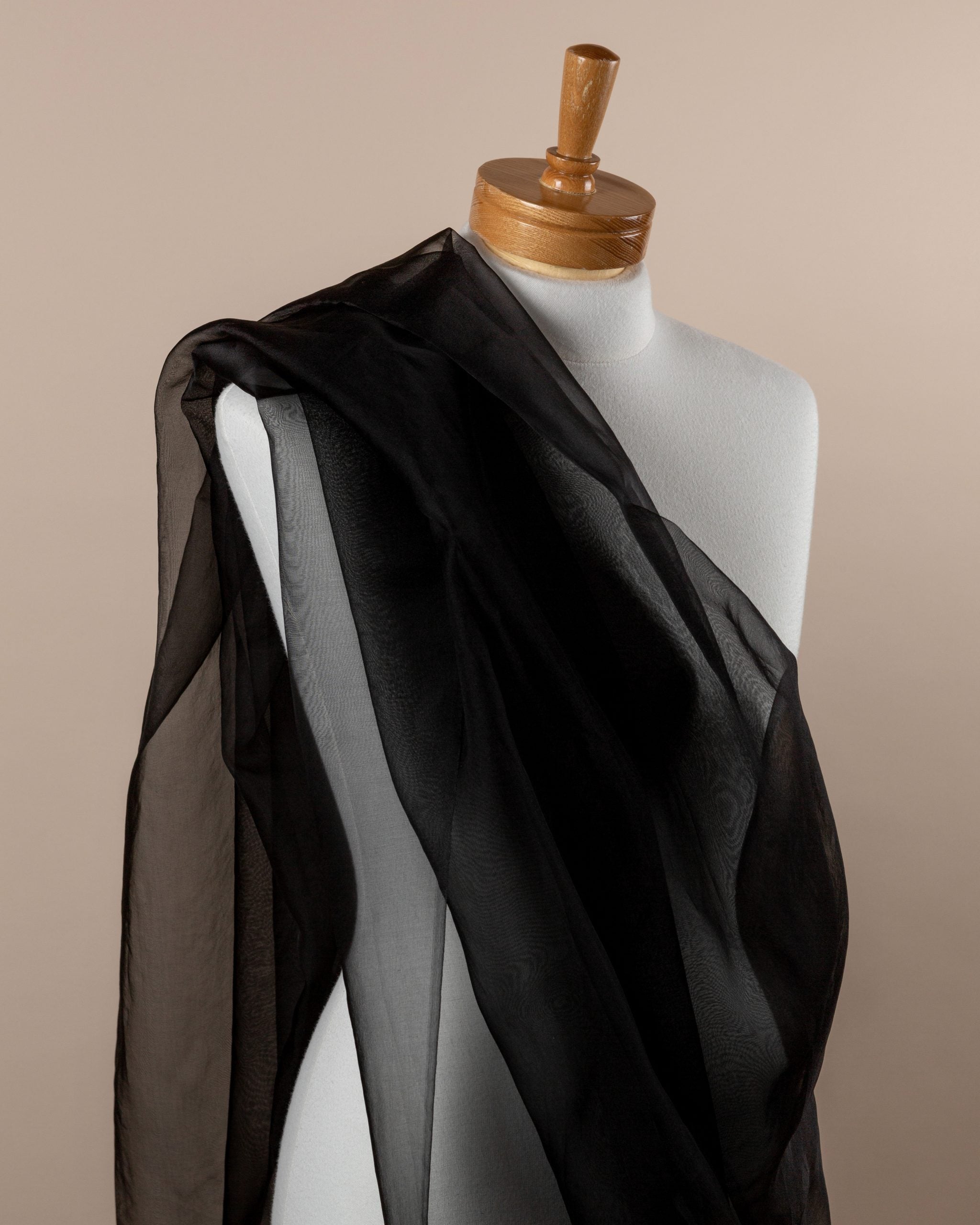 Black silk organza draped over a mannequin against a beige background